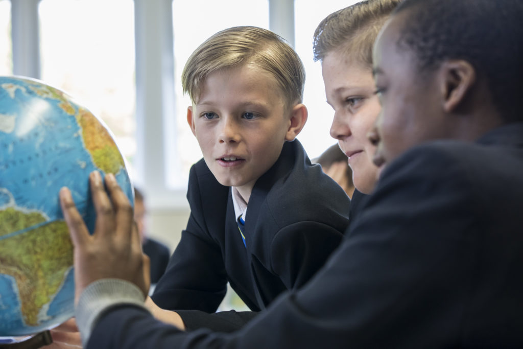Three boys looking closely at a 3D Globe during a Geography class