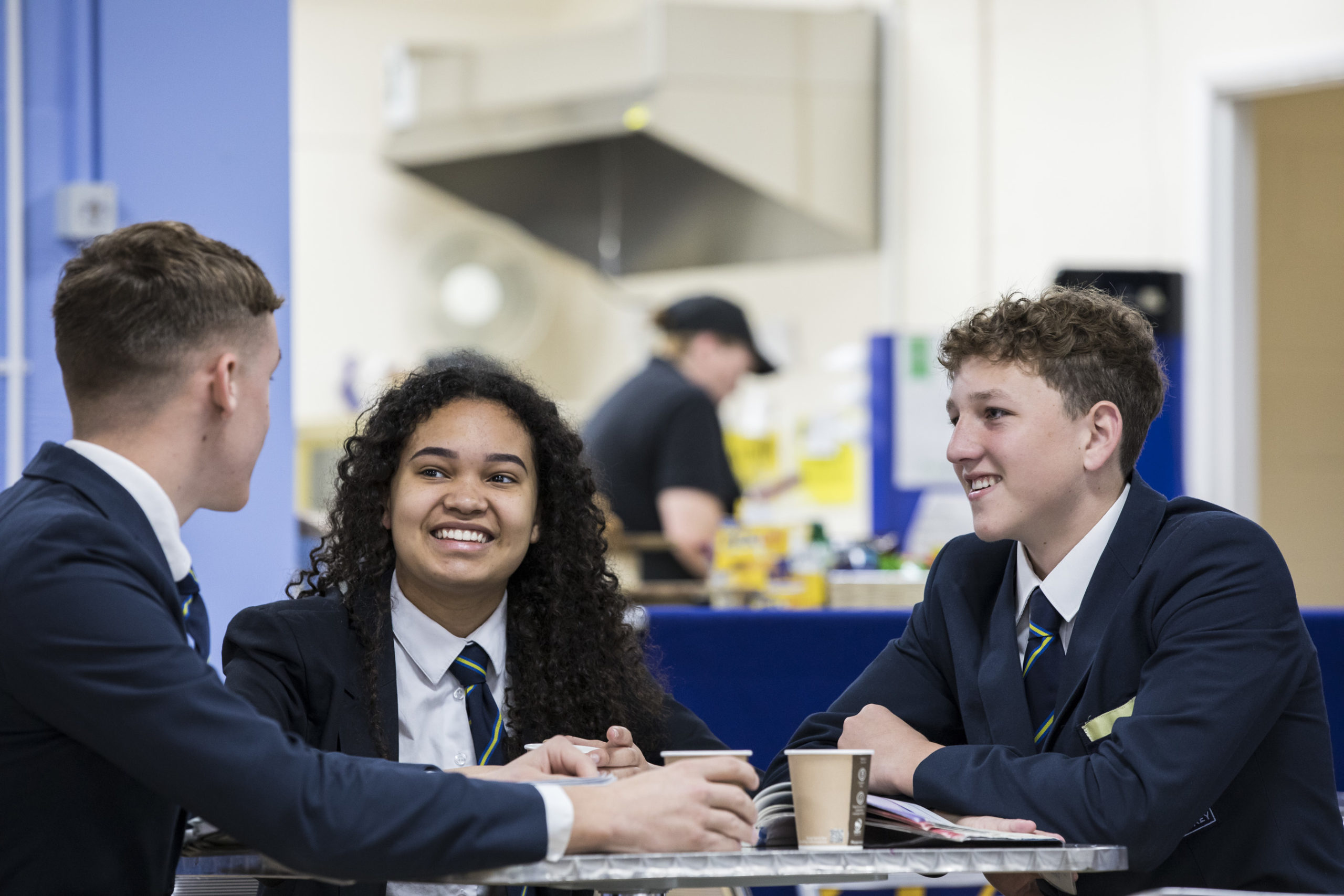 Two boys and One female sixth form students laughing and talking in the school canteen