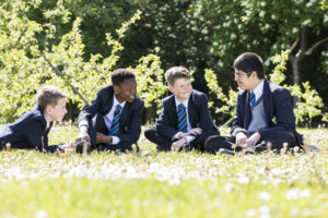 Four boys sitting on the school field while smiling and talking to each other