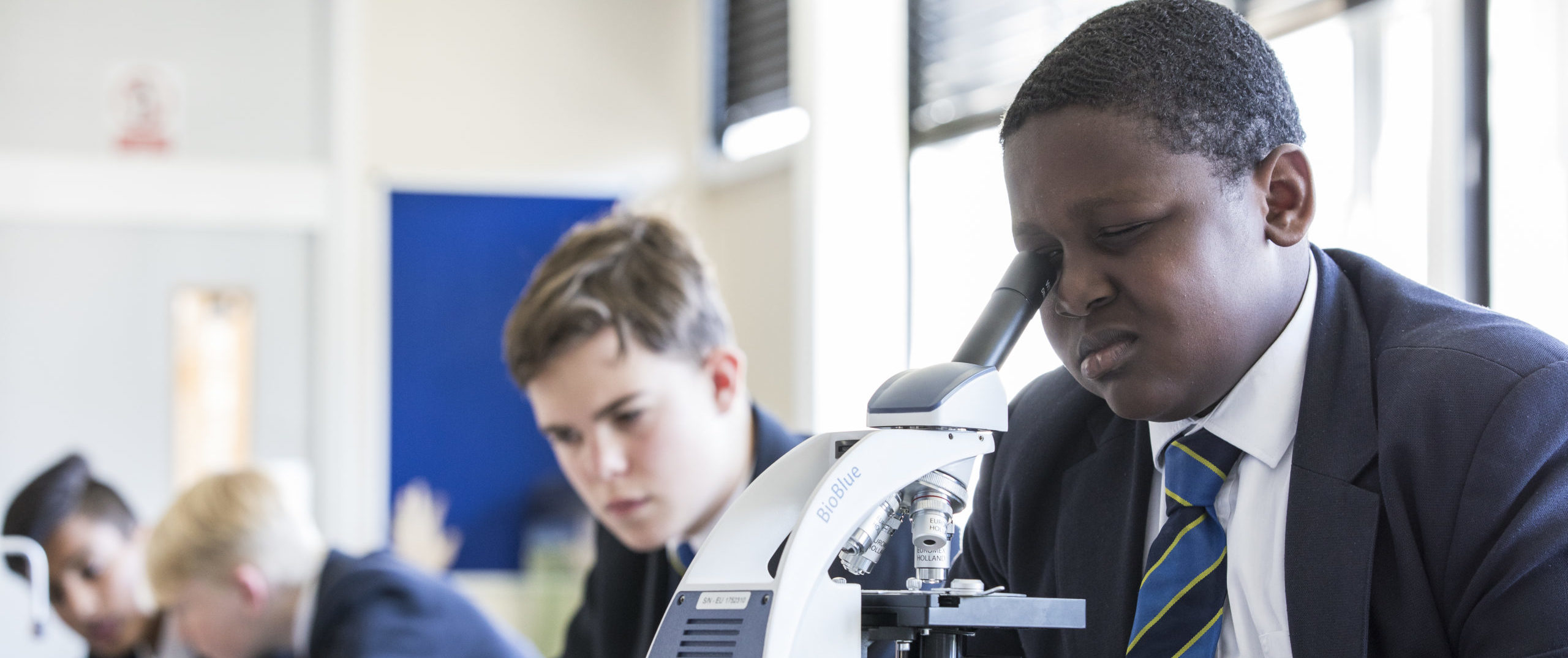 A boy looking into a microscope during a Biology class