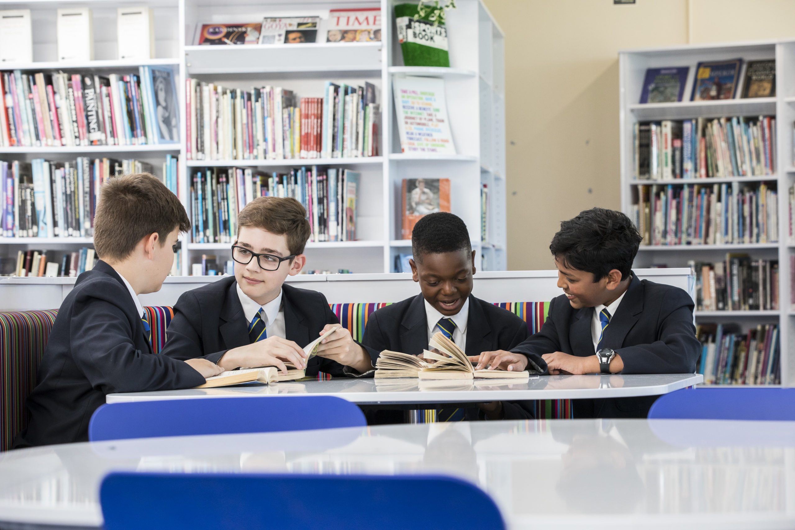 Four boys sitting around a table talking and laughing in the library