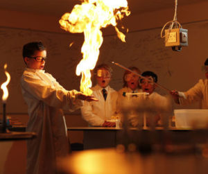 A boy wearing fire resistant gloves with flame coming out of hands during a chemistry class