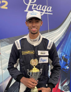 A former SJWMS student, Ruben, can be seen holding a Formula 1 racing trophy and wearing his uniform at an F1 event.