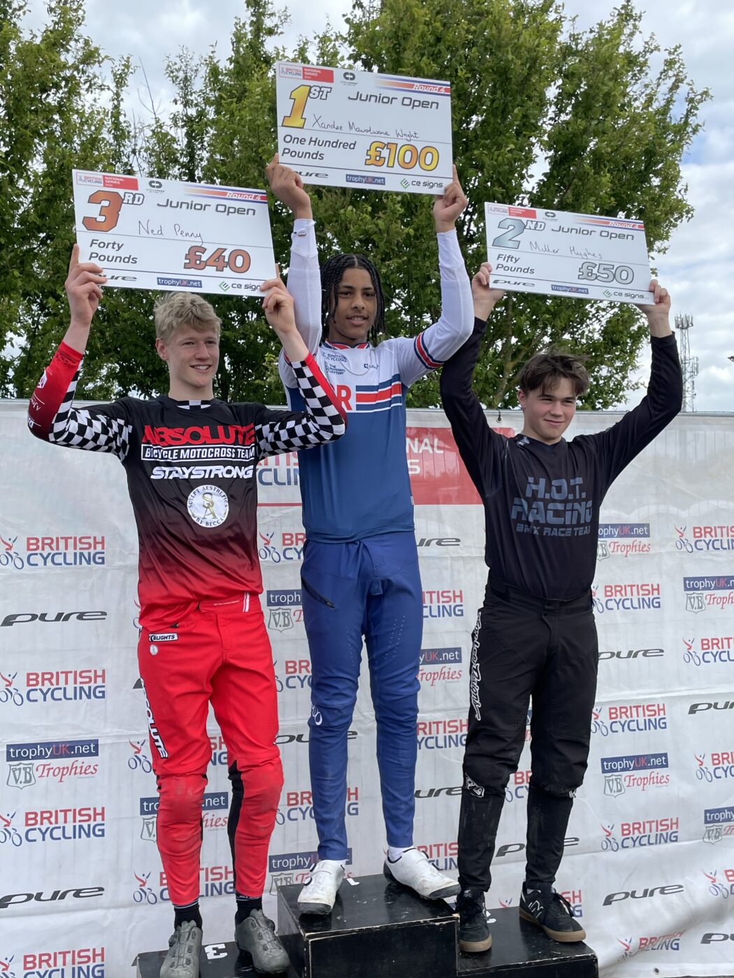 Three young men are pictured standing alongside each other on a pedestal, in 3rd, 2nd and 1st place, at the National BMX Championships.