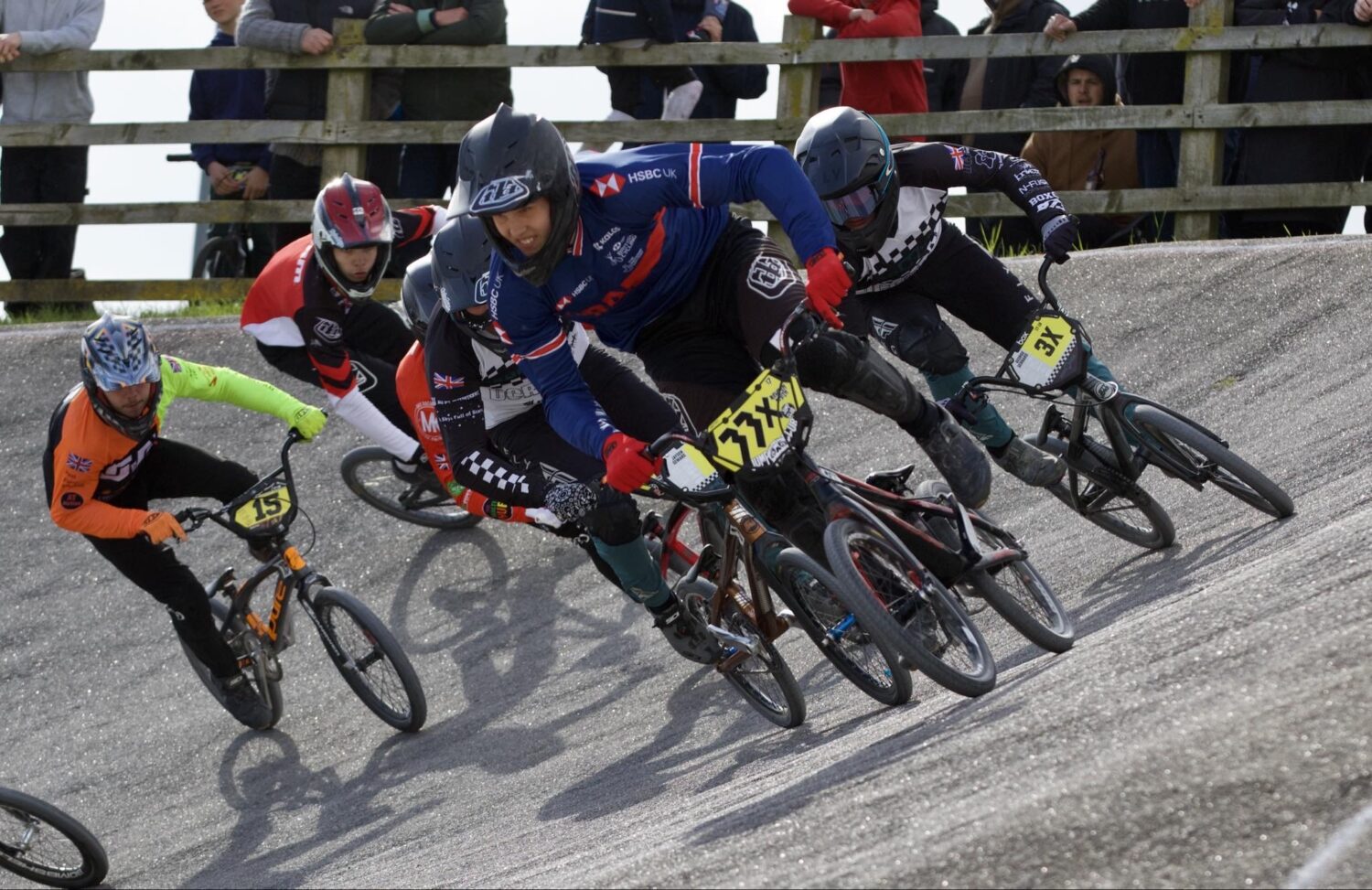 A group of young men are pictured racing each other on BMX bicycles along a race track.