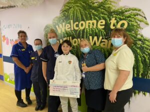 A boy holding a giant cheque is picture with hospital staff wearing masks